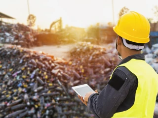 man wearing a yellow hard hat and high vis jacket looks at waste pile