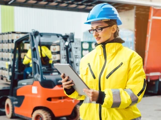lady wearing a fluorescent jacket and hard hat looking at her tablet